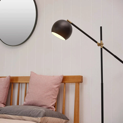60-Inch Floor Lamp With Matte Black Finish, Brass Pivot, Metal Shade, Inline On Off Foot Switch beside a wooden bed in a bedroom.