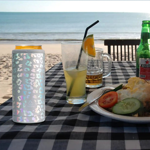 Laser Leopard Skinny Can Cooler Made With Double Wall Vacuum Insulated Stainless Steel To Keep Your Twelve Ounce Tall Boys Frosty All Night Long Perfect Bridesmaid Party Favors That Truly Hit Different on a beach table with drinks.