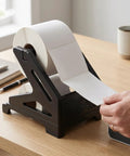 Thermal Label Holder For Rolls And Fan Fold Labels on desk with hand pulling label from stand, ideal for home office use.