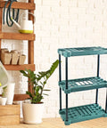 Heavy Badass Broom And Mop Organizer Rock Solid Corner Rack With Hella Durable Polypropylene Shelves And Reinforced Iron Frame Top Shelf Laundry Room Garage Cleaning Tools Storage Rack displayed with gardening tools and plant.