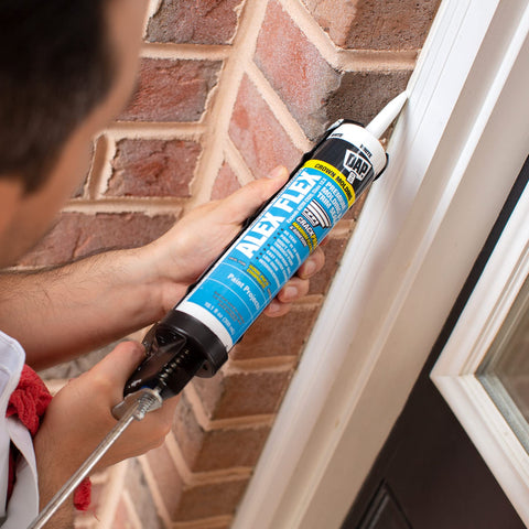 Applying Alex Flex Premium Molding And Trim Siliconized Sealant White 10.1 Oz on exterior window trim for flexible adhesion.