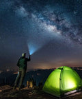 A person using a Tactical LED Flashlight With Aluminum Alloy Body, Zoomable Beam, Up To 1,000 Feet Reach next to a tent under a starry sky.