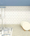 Peel And Stick Backsplash Tile Kit 12x12 Off White Subway Tiles With Grey Grout 10 Sheets Easy DIY No Mess Eco Friendly Kitchen Upgrade Self Adhesive Tiles With Shiny Finish For Quick Remodel installed in kitchen setup, glossy white tiles with grey grout near sink and dish rack.