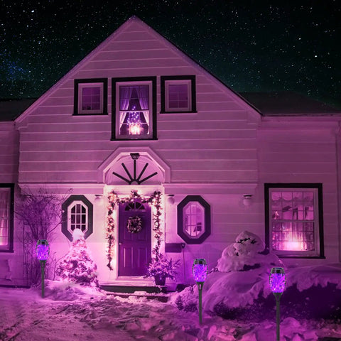 Purple Solar Tiki Torches Outdoor Lights 12 Pack With Flickering Flame illuminate a snow-covered yard in front of a house at night.