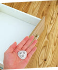 Heavy Duty Peel And Stick Caster Wheels 8 Pack Steel Rolling Casters in hand above empty drawer on wooden floor.