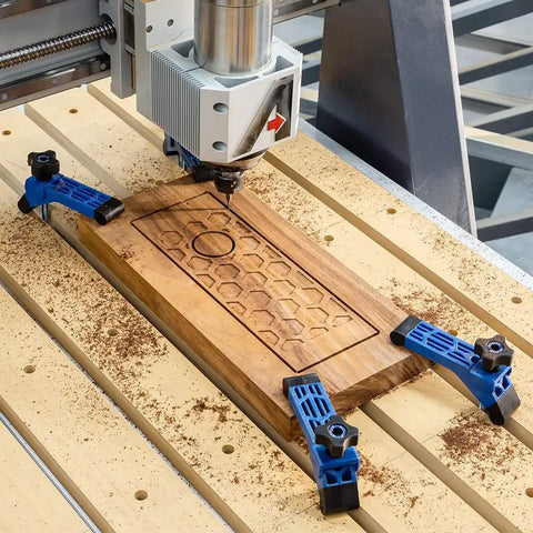 CNC router machine with Bit Saver Hold Down Clamps, five and a half inch long by one and a quarter inch wide, on wooden workpiece.