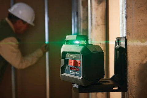 Green Beam Self Leveling 360 Degree Cross Line Laser with L Bracket mounted on wall at job site, worker in background