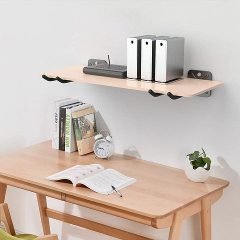 Wall-mounted shelf with books and decor above a desk setup with clock and plant, illustrating organized wall storage.
