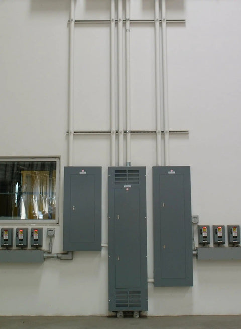 Electrical panel setup in industrial building with wiring conduits leading to multiple control boxes on the wall.