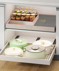 Kickass Pull Out Cabinet Organizer With No Sweat Adhesive Mount For Kitchens Expandable From Fourteen To Twenty One Inches Wide And Seventeen To Twenty Four Inches Deep Easy DIY Placement Total Space Saver For Cluttered Drawers showing filled jars and cookware in neat drawer layout.