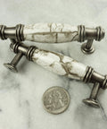Antique-style cabinet pulls with marble handles next to a coin for size comparison on a gray surface.