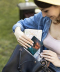 Woman placing map and postcard inside large black handbag outdoors.