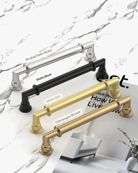 4 kitchen cabinet handles in brushed satin nickel, matte black, matte gold, and champagne bronze finishes on a marble surface.