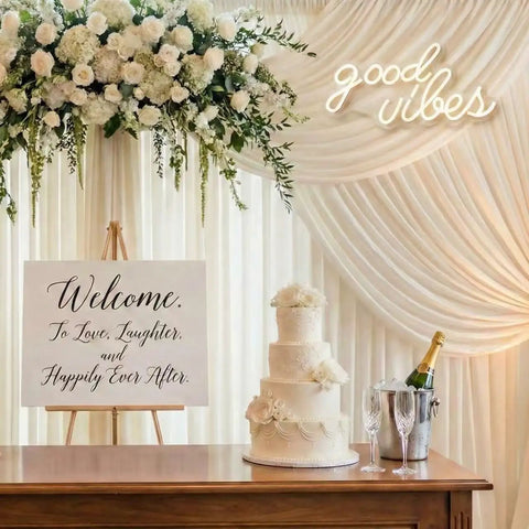 Good Vibes Neon Sign LED Wall Decor With Warm White Glow For Living Room And Weddings Boho Minimalist Modern Farmhouse Backdrops USB Powered 3D Art Gift 16.1x8.3 Inch displayed at wedding reception with floral arrangement and cake.
