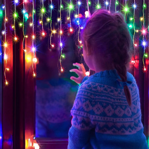 Child gazing at Ultra Bright 1280 LED Christmas String Lights 131 Ft With 240 Drops, 8 Modes, multicolor glow in window reflection.