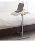 Slick Height Adjustable Laptop Table With Smooth Rolling Locking Casters Premium Couch Side Stand Heavy Duty Wood Finish Foldable Computer Cart For Lazy Day Lounging by the bed with laptop setup.