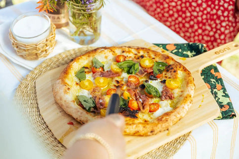 Heavy Duty 14 Inch Bamboo Pizza Peel And Wooden Spatula Paddle For Backyard Cookouts with pizza on a rustic serving board.