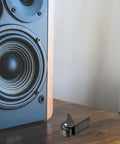 Two Pack Black Right Angle Fixed Casters With L Bracket Plates Non Swivel Rubber Wheels next to a loudspeaker, showcasing their heavy-duty design.