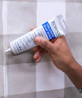 Hand using Seam Repair Adhesive for Wallpaper Tears and Loose Edges Sealer White 3 Ounce Tube with Applicator Nozzle