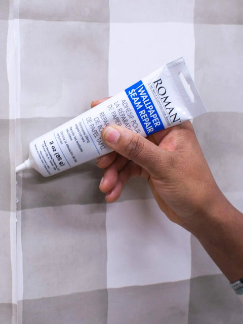 Hand using Seam Repair Adhesive for Wallpaper Tears and Loose Edges Sealer White 3 Ounce Tube with Applicator Nozzle