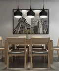 Dining room with wooden table and chairs, black pendant lights, and framed cityscape artwork on wall.