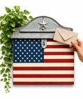 Vintage Farmhouse Post Box With Folding Top For Home Decor Nostalgic Charm With Grab Worthy White Horizontal Style Durable Metal Craft Classic Country Vibe with American flag pattern, beside green plant and hand inserting mail, 15.9 Inch Tall By 11 Inch Wide Perfect Corner Accent.