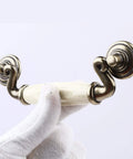 Close-up of a Set Of 4 4.5 Inch Ceramic Drop Handle Drawer Pulls In Antique Bronze Finish, held by gloved hand, showing ivory cream ceramic detail.