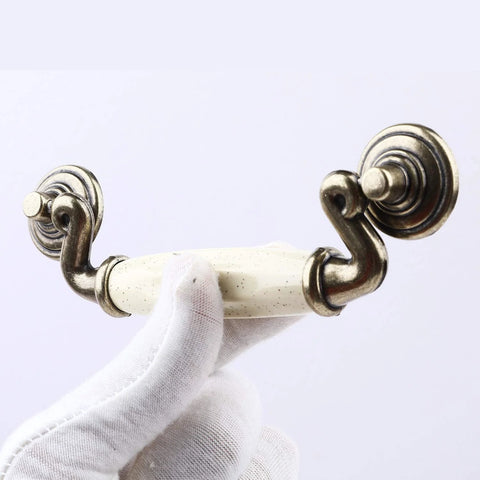Close-up of a Set Of 4 4.5 Inch Ceramic Drop Handle Drawer Pulls In Antique Bronze Finish, held by gloved hand, showing ivory cream ceramic detail.