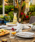 White gnome table torch on outdoor patio table set for dining, featuring flame lit lantern with fiberglass wick and snuffer, surrounded by dishes.