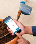 Person using phone app to control Bluetooth Hose Timer on outdoor tap. Bluetooth Hose Timer You Control From Your Phone No Fuss App Controlled Irrigation For Lawn And Garden Battery Powered Easy Install On Outdoor Tap Programmable Single Zone Watering Schedule.