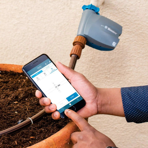 Person using phone app to control Bluetooth Hose Timer on outdoor tap. Bluetooth Hose Timer You Control From Your Phone No Fuss App Controlled Irrigation For Lawn And Garden Battery Powered Easy Install On Outdoor Tap Programmable Single Zone Watering Schedule.