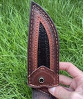 Close-up of rugged leather knife sheath for fixed blade with buckle, shown in hand outdoors.