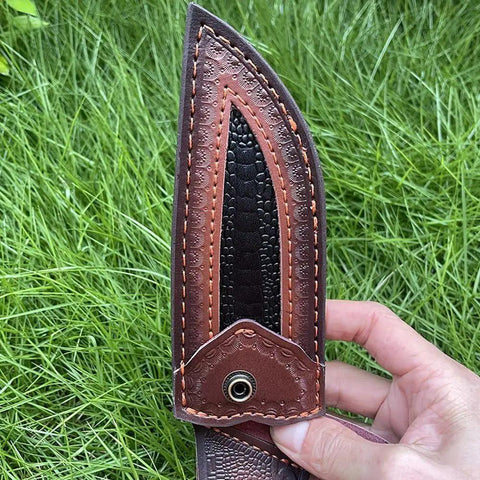 Close-up of rugged leather knife sheath for fixed blade with buckle, shown in hand outdoors.