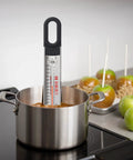 Curved Candy And Deep Fry Thermometer With Pro Grade Stainless Steel Paddle in pot with caramel apples in background