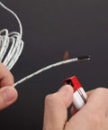 Close-up view of white braided K-type thermocouple wire with blue tracers, 3 m length, being cut on a dark surface