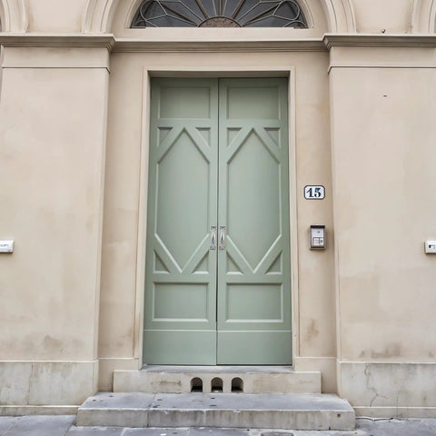 Large light green double doors with decorative panels and arched window at the top, framed by beige stucco wall.