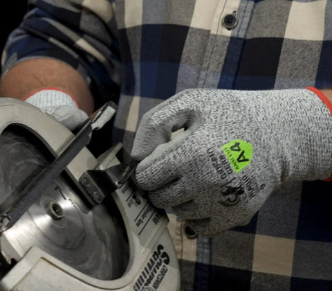 Top Shelf ANSI A4 Cut Resistant Work Gloves With Smooth Polyurethane Grip And Durable DuraBlend Shell Built Tough For Grease Monkey Tasks Providing Rock Solid Level 5 Abrasion And Level 4 Puncture Protection In Large Fits Bulk Pack Of 24 Pairs, worn while handling a circular saw.