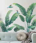 Lush Tropical Wall Stickers Set With Monstera Leaf And Palm Leaves Banana Leaf And Bird Mural For Bedroom Or Living Room Totally Easy Peel And Stick Decor To Create A Nordic Green Jungle Vibe In Your Space on white wall behind sofa
