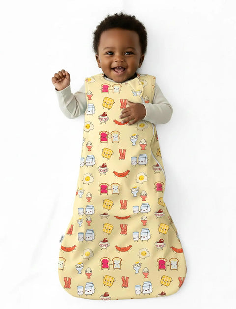 Smiling baby wearing Soft Bamboo Viscose Baby Sleep Sack 1.0 TOG For 0-6 Months, Breakfast Friends, yellow with breakfast print.