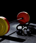 Barbell with red and yellow weight plates on gym floor, kettlebells beside it, heavy duty 2 inch barbell clamps quick release pair locking Olympic weight plate collars red and black easy weight swaps for powerlifting home gym fitness training clips