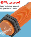 Close-up of SZC M30 capacitive proximity sensor switch, orange housing, IP65 waterproof, showing water resistance in use.
