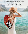 Woman by lake with 2 In 1 Travel Blanket And Pillow Set With Convertible Pillowcase Lightweight Microfleece Comfort For Airplane And Road Trips On The Go Includes Hand Luggage Sleeve And Backpack Clip Checkered Black clipped to red backpack.