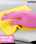 Close-up of magenta nitrile disposable glove wiping a car hood with a yellow microfiber cloth; SafeSkin logo visible