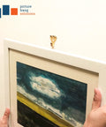 Hands hanging a framed painting using heavy duty picture hangers with nails, 50 lb wall hooks for drywall and plaster, pack of 20.