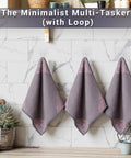 Three gray microfiber cleaning towels with pink corner floral design hanging on a rack in a marble-tiled kitchen