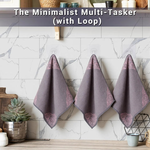 Three gray microfiber cleaning towels with pink corner floral design hanging on a rack in a marble-tiled kitchen
