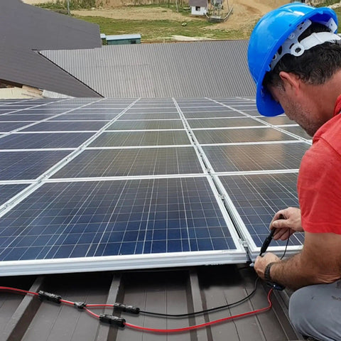 Installation of Plug And Play Solar Panel Extension Cable 20FT 14AWG Waterproof on rooftop solar array by technician in blue helmet.