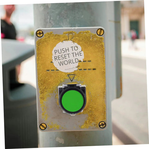 Close-up of a green elevator button with "Push to Reset the World" sticker, featuring 4 Pack Round Elevator Button Protector Covers Easy Install Plastic Dustproof Power Switch Guard Caps For Public Buildings Push Button Safety Covers Compatible With Washing Machines And Dishwashers.