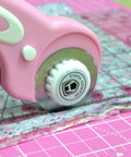 Close-up of pink 45mm rotary cutter in use with ergonomic handle on fabric, part of 45mm Rotary Cutter Set With Ergonomic Handle, Five Extra Rotary Blades And Ten Replacement Blades, A3 Cutting Mat, Quilting Ruler, Craft Knife And 20 Sewing Clips For Crafting, Sewing, Patchwork And DIY Projects In Pink.