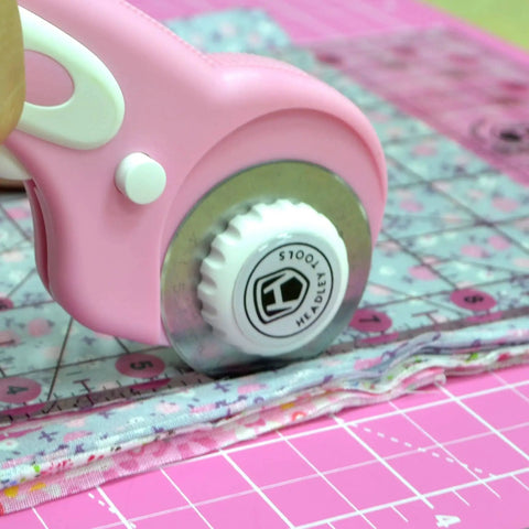 Close-up of pink 45mm rotary cutter in use with ergonomic handle on fabric, part of 45mm Rotary Cutter Set With Ergonomic Handle, Five Extra Rotary Blades And Ten Replacement Blades, A3 Cutting Mat, Quilting Ruler, Craft Knife And 20 Sewing Clips For Crafting, Sewing, Patchwork And DIY Projects In Pink.
